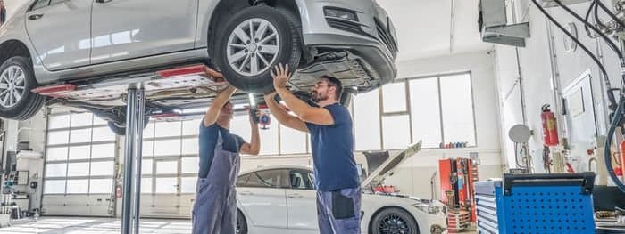 Two mechanics working underneath a car raised on a workshop lift